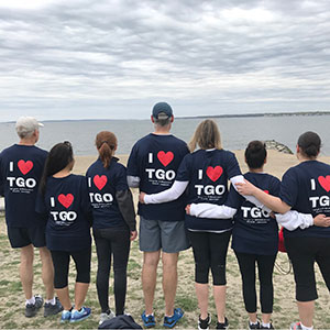 A group of Tollgate Orthodontics employees standing in front of the ocean wearing shirts that say IHeartTGO.