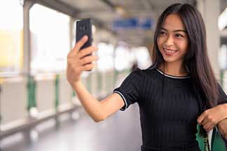 A smiling woman holding a cellphone in front of her.