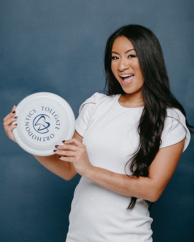 A smiling woman holding a frisbee branded with the Tollgate Orthodontics logo.